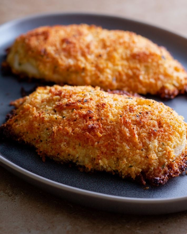 Crispy Keto Parmesan Chicken - baked keto crispy chicken served whole on a dark plate, with a coarse, browned golden crust