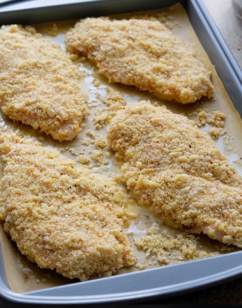 Keto Chicken Parmesan Prep — breaded low-carb chicken breast cutlets arranged on a parchment-lined baking tray