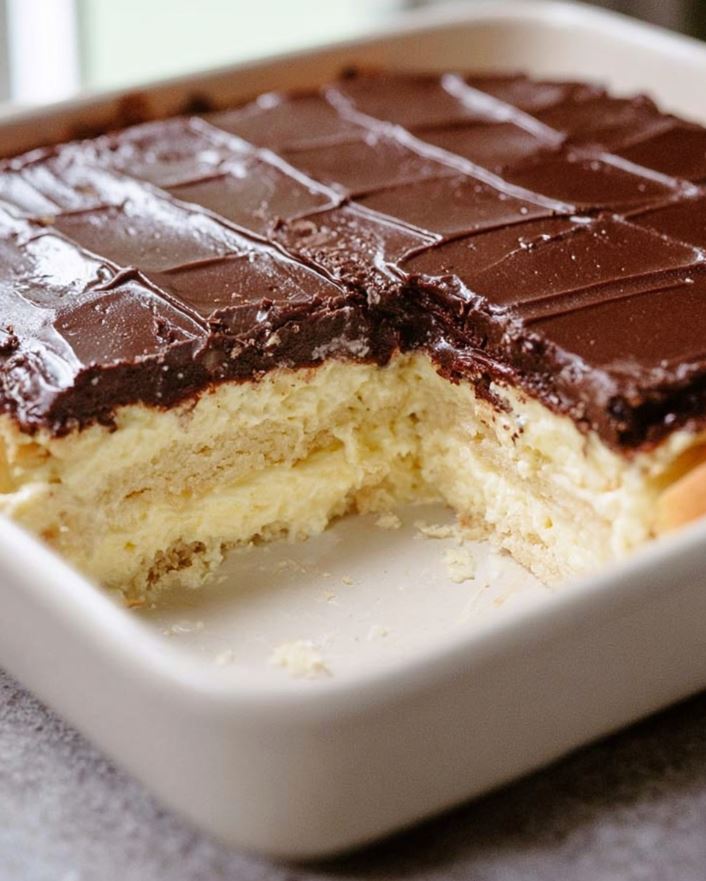 Keto Eclair Cake - The dessert in a white baking dish, showing the cut chocolate surface and visible creamy layers after chilling