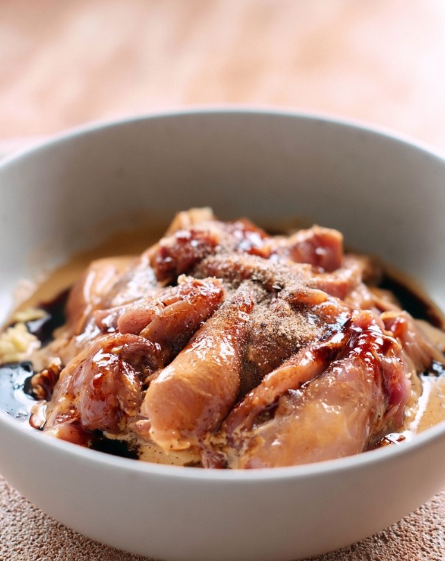 Keto Chicken Satay - Raw chicken thigh strips resting in a white bowl, thoroughly coated in a creamy coconut and dark soy satay marinade.