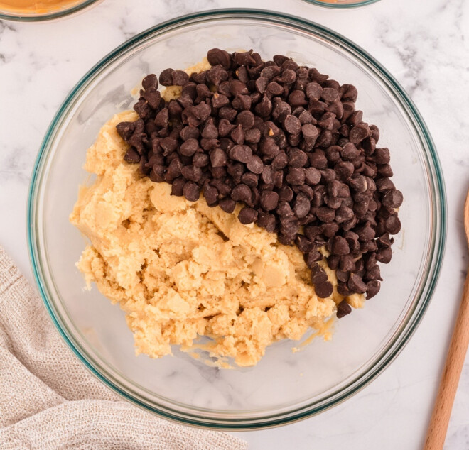 Gooey Low-Carb Caramel Chocolate Chip Cookie Bars — Chocolate caramel cookie bar dough in a glass bowl with dark chocolate chips before mixing.