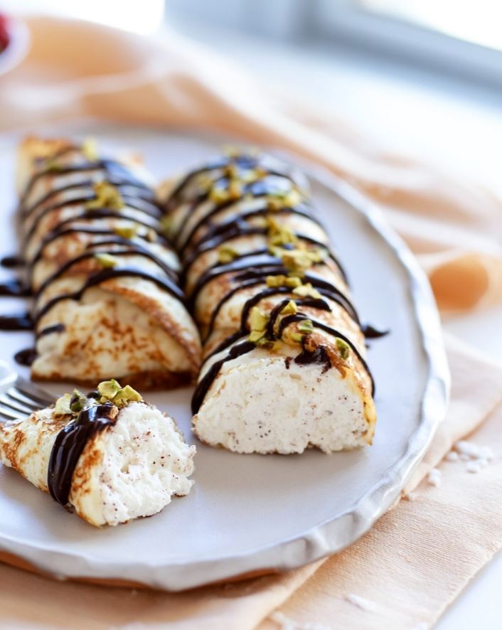 Keto Cannoli Stuffed Crepes - cut open on a white ceramic plate revealing a creamy white filling under a glossy chocolate drizzle