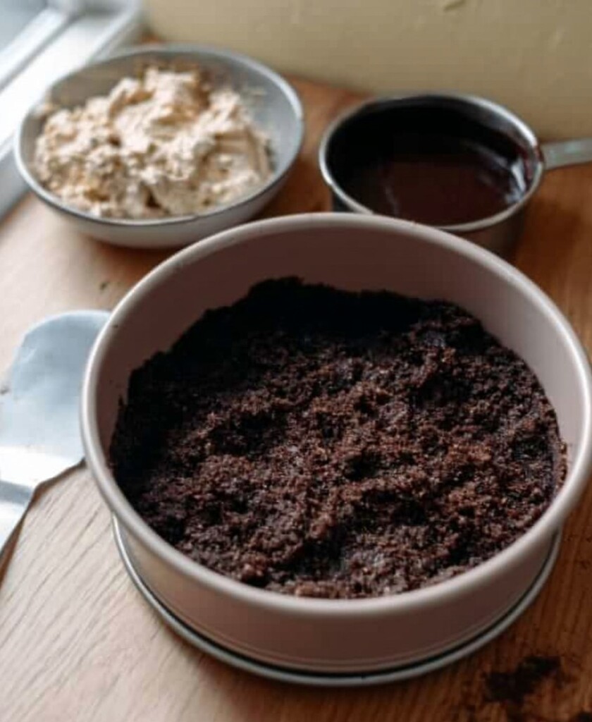 Keto Dirt Cake Prep - Chocolate almond crumb base pressed into a springform pan with peanut butter and cream cheese filling ingredients nearby.