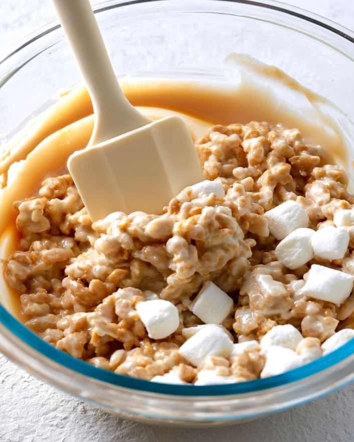 Mixing the cookies - gently folding the crisp cereal and marshmallows into a smooth, creamy peanut butter coating inside a glass bowl