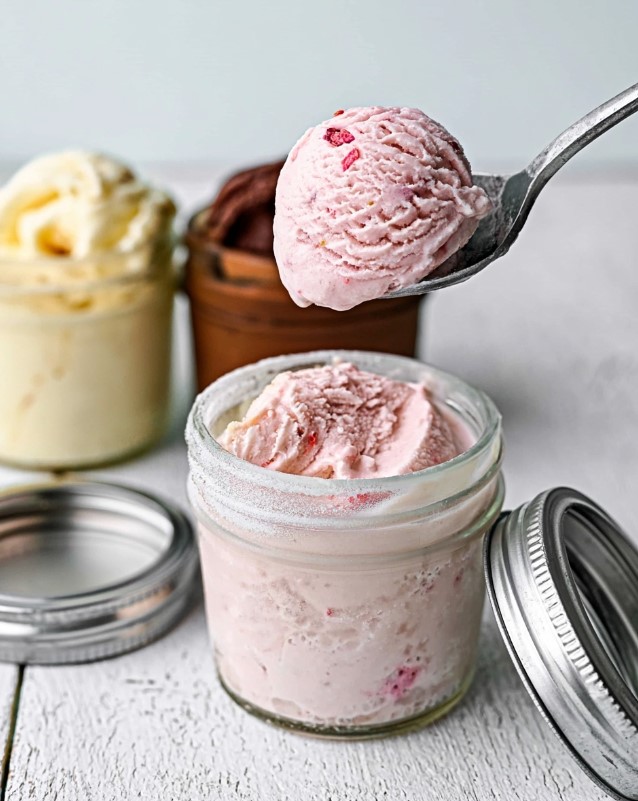 Serving Keto Mason Jar Ice Cream - Strawberry ice cream being scooped with a metal spoon from a glass jar, showing a smooth, speckled pink texture
