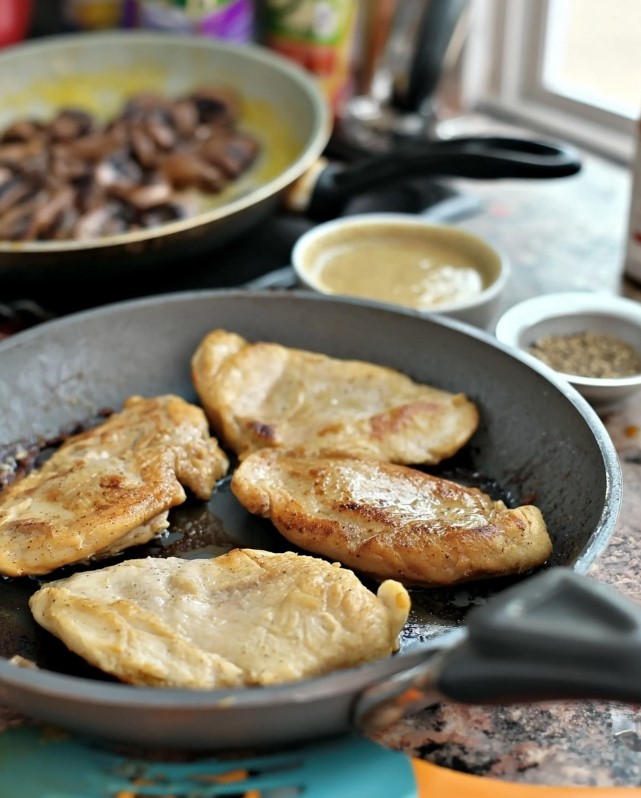 Keto Smothered Chicken Breast - Keto chicken breasts browning in a grey skillet until they develop a glossy, golden surface.