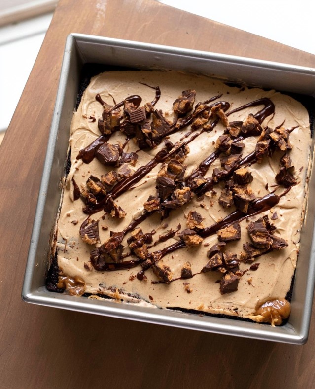Keto Chocolate Peanut Butter Cake - Square baking pan filled with chocolate cake, generously frosted with smooth peanut butter cream, chocolate drizzle, and candy pieces