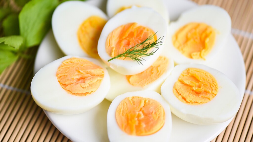 Hard boiled egg halves on a white plate with fresh greens and a sprig of dill.