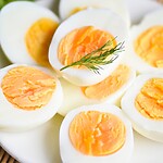 Hard boiled egg halves on a white plate with fresh greens and a sprig of dill.