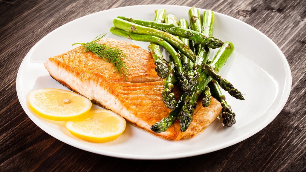 Grilled salmon served with asparagus and lemon slices on a white plate.