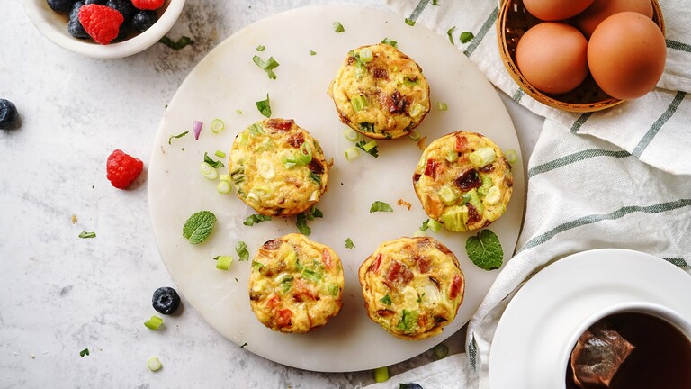 Low-carb egg muffins with vegetables served on a white plate beside eggs, berries, and tea.