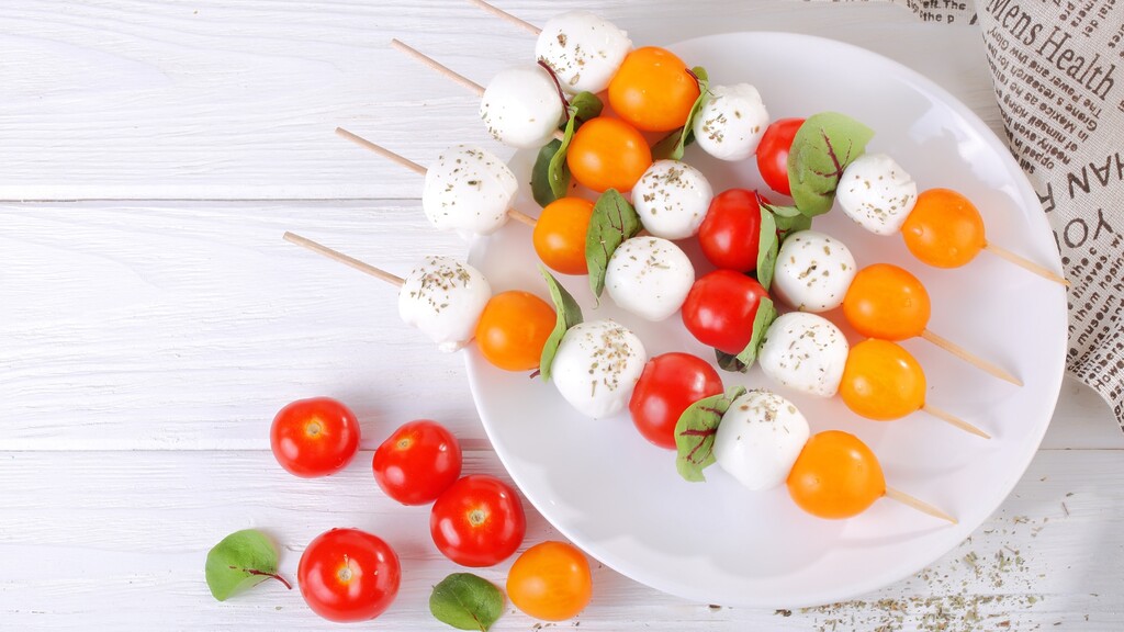 Tomato and mozzarella skewers with basil on a white plate.