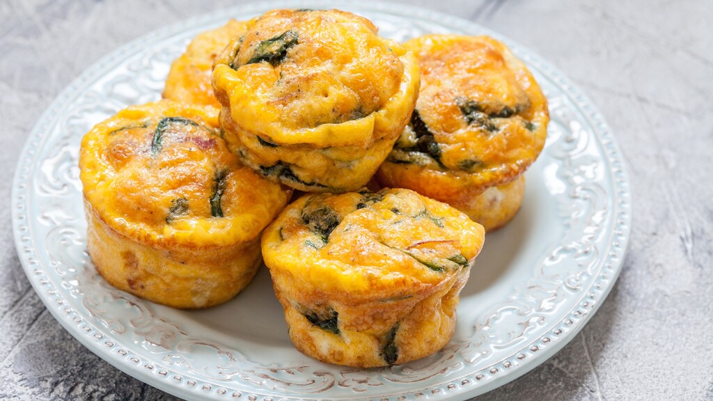 Egg muffins on a decorative plate with spinach and melted cheese.