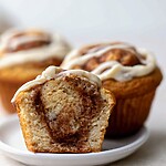 Protein cinnamon roll muffins topped with cream cheese glaze showing a soft crumb and cinnamon swirl inside