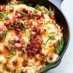 Melted cheddar and Monterey Jack cheese bubbling over chicken tenders with chopped bacon and scallions in a cast iron skillet