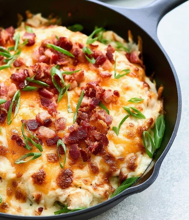 Melted cheddar and Monterey Jack cheese bubbling over chicken tenders with chopped bacon and scallions in a cast iron skillet
