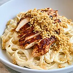 Grilled chicken alfredo over creamy fettuccine topped with golden panko in a white bowl