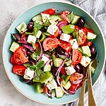 Classic Greek salad served in a green ceramic bowl with tomatoes, cucumbers, peppers, olives, feta, and mint leaves