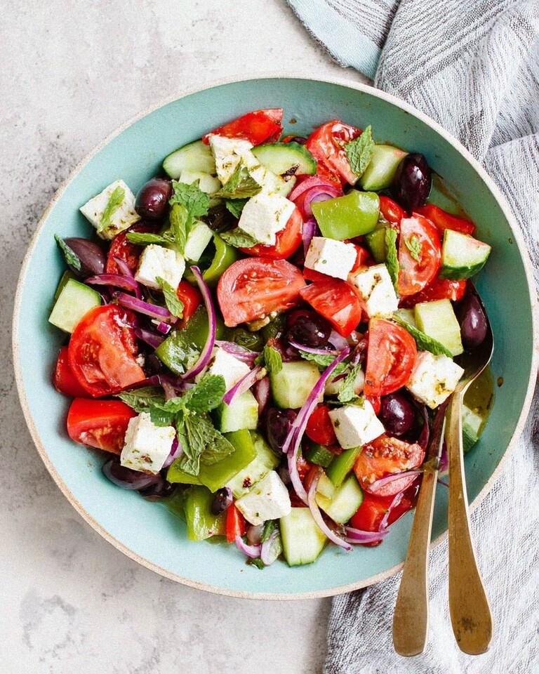Classic Greek salad served in a green ceramic bowl with tomatoes, cucumbers, peppers, olives, feta, and mint leaves