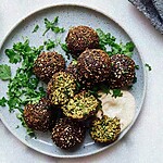 Crispy herb and sesame falafel served on a ceramic plate with a creamy sauce and fresh chopped parsley