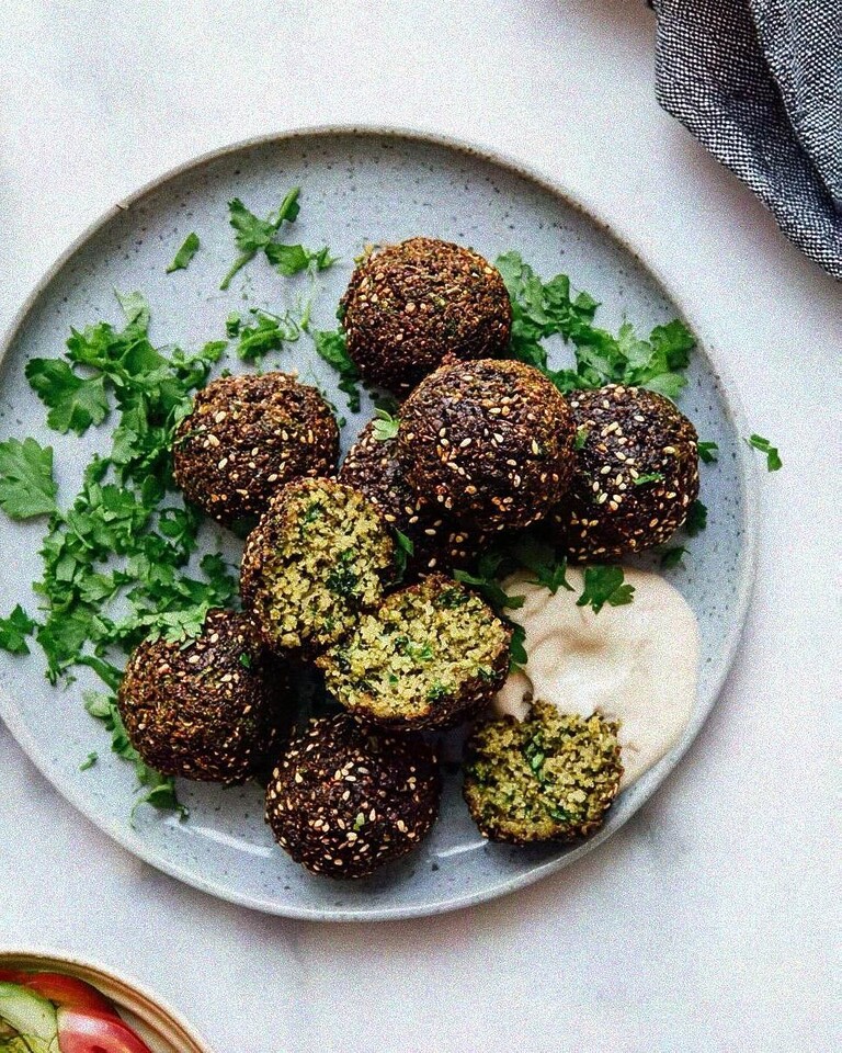 Crispy herb and sesame falafel served on a ceramic plate with a creamy sauce and fresh chopped parsley