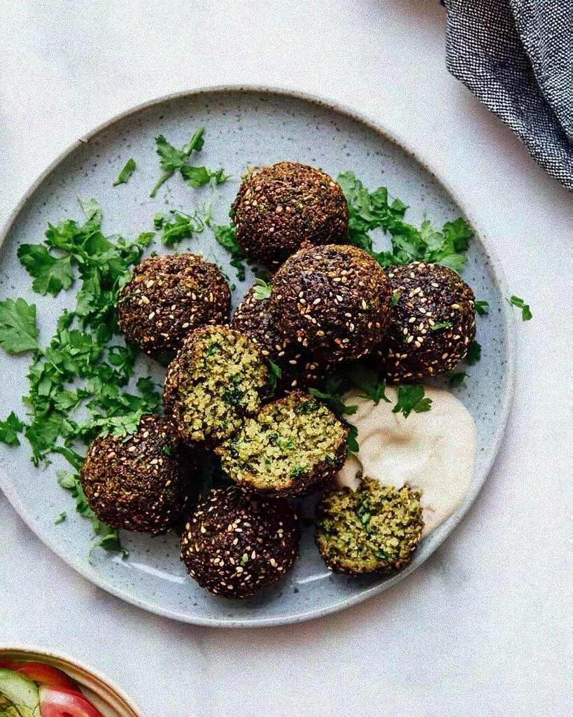 Crispy herb and sesame falafel served on a ceramic plate with a creamy sauce and fresh chopped parsley