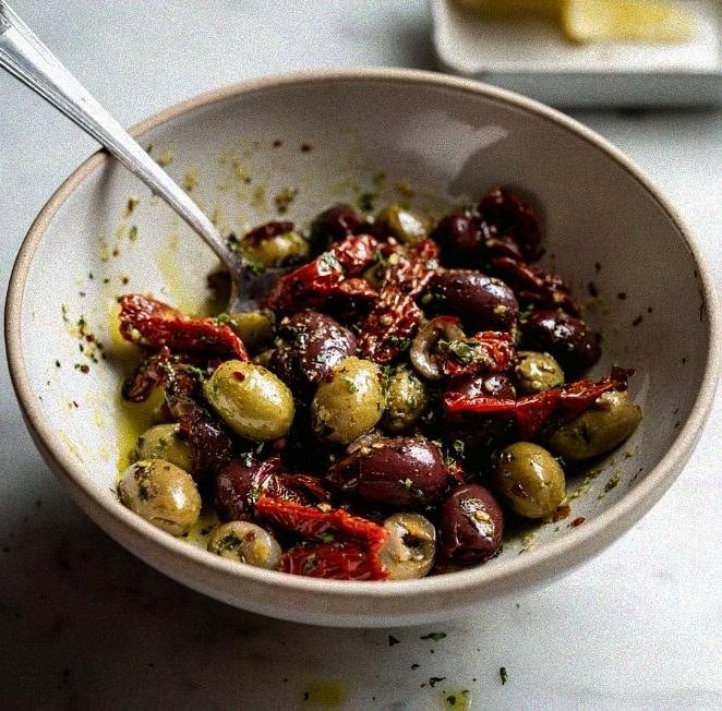 Halved olives, sun dried tomatoes, garlic, and herbs tossed together in a small bowl