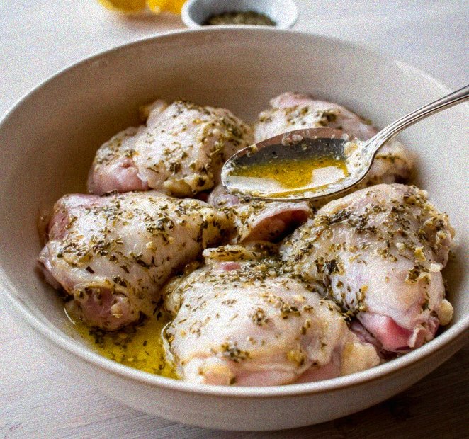 Raw chicken thighs coated in a lemon herb oil marinade inside a deep bowl