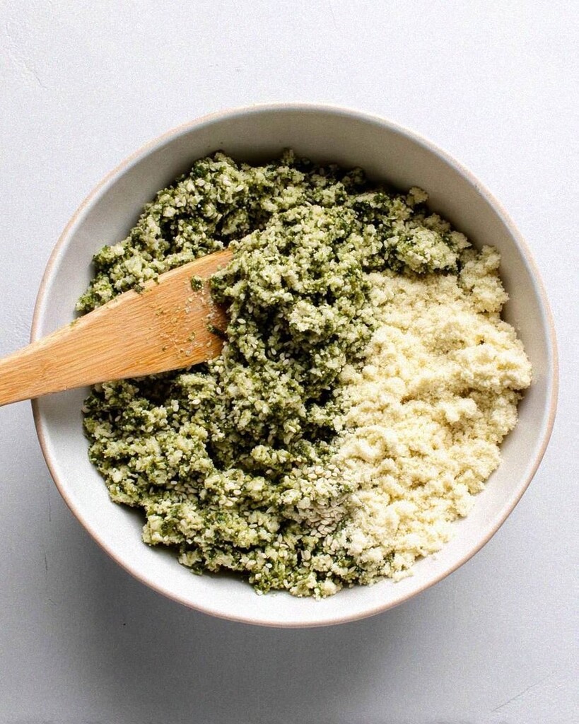 Coarse green falafel mixture with toasted sesame seeds being stirred in a light mixing bowl