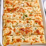 Cheesy garlic breadsticks arranged on a white rectangular platter topped with fresh green herbs