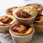 Baked cinnamon roll muffins resting in white liners on a wire rack with domed browned tops