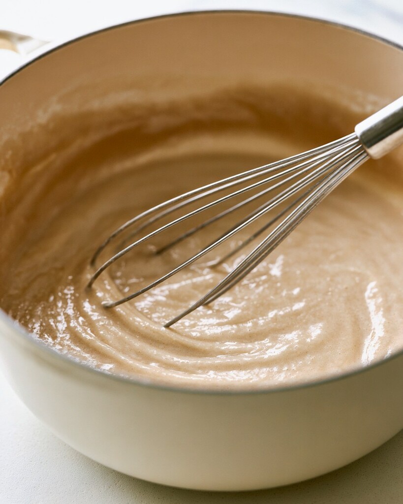 Light-colored macaroni and cheese sauce base being whisked in a heavy pot
