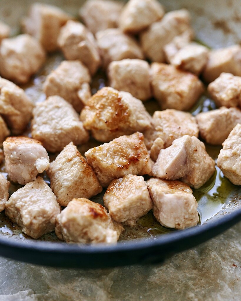Cubed chicken browning in a black skillet