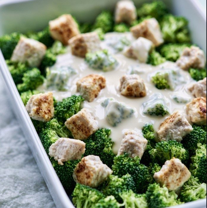 Creamy Alfredo sauce poured over chicken and broccoli in a baking dish