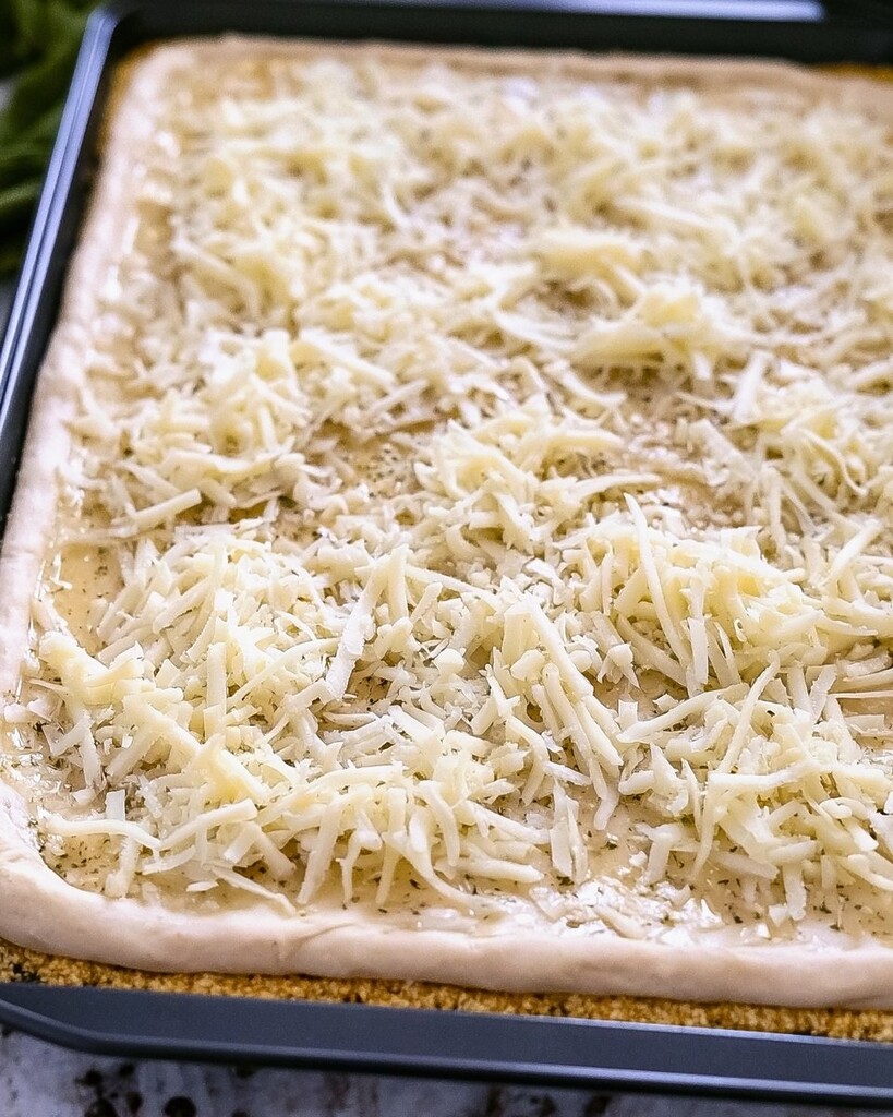 Shredded mozzarella and Parmesan cheese covering stretched dough in a black baking pan