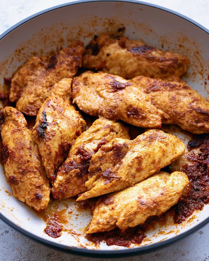 Browned chipotle chicken cutlets searing in a wide skillet with dark spiced pan drippings