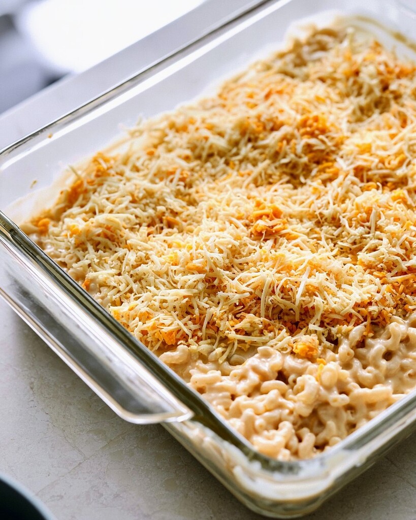 Glass baking dish filled with creamy macaroni and topped with a thick layer of shredded cheese before baking