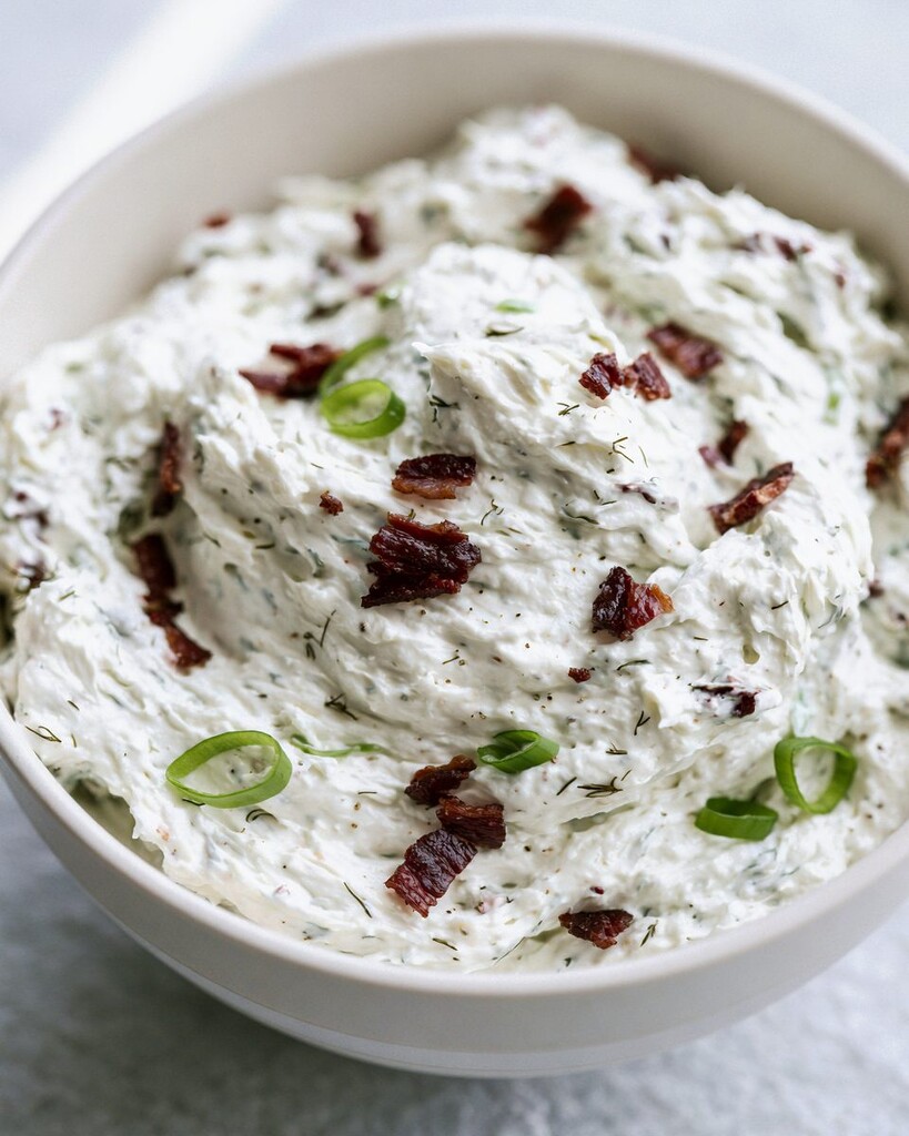 Softened cream cheese mixed with chopped bacon, scallions, and dried herbs in a white bowl