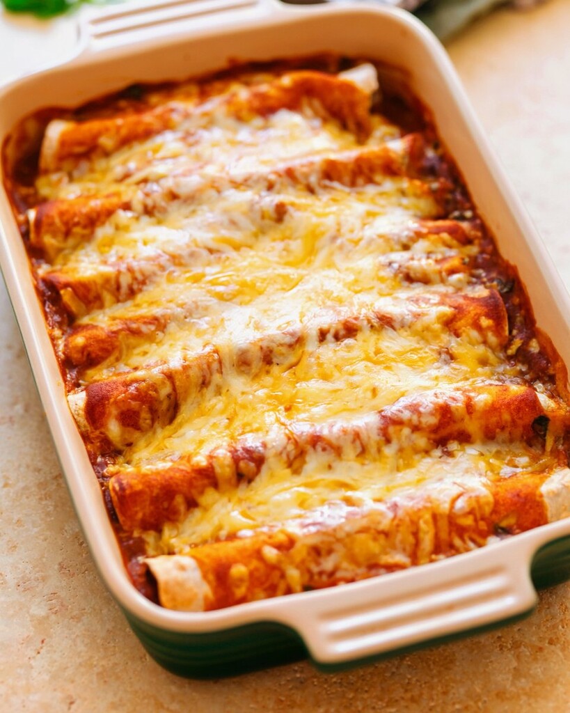 Chicken enchiladas nestled in a baking dish, covered in red sauce and a generous layer of shredded cheese before baking