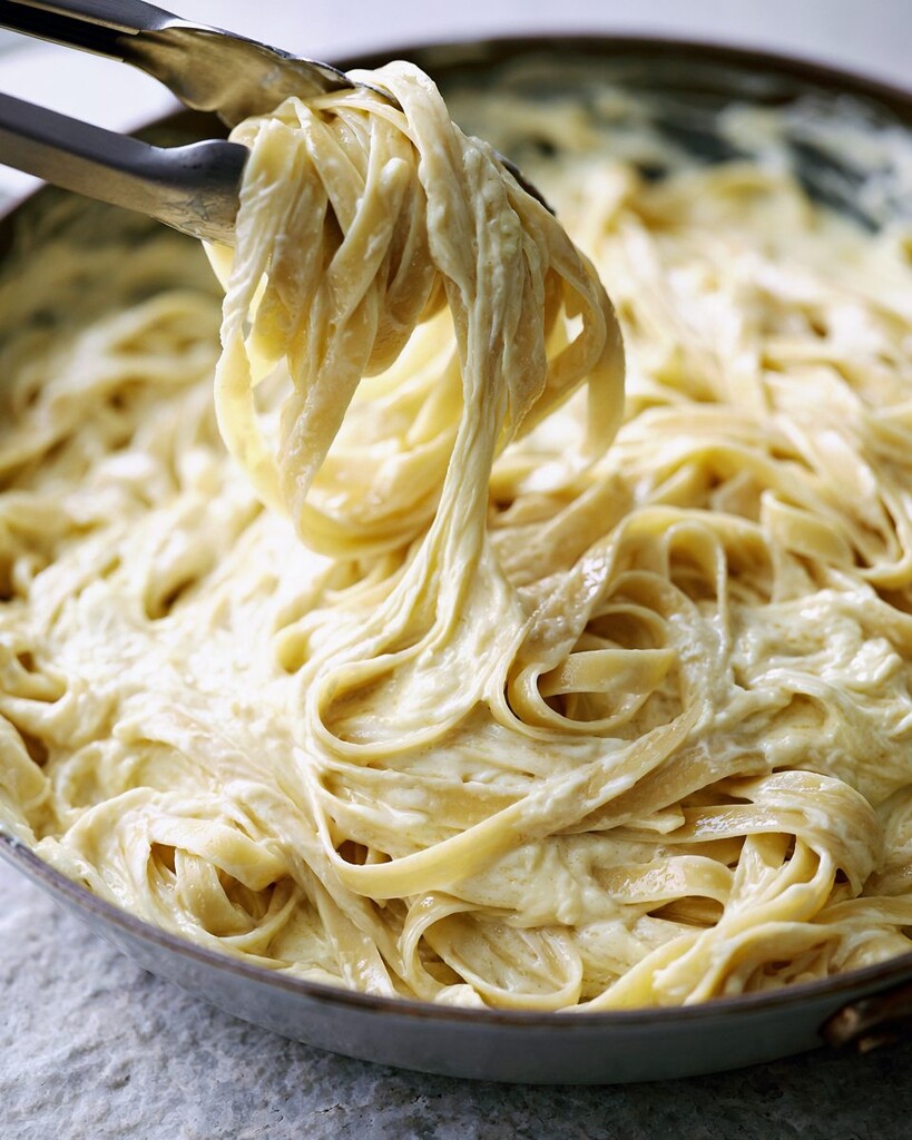 Fettuccine noodles being tossed with tongs in a creamy alfredo sauce