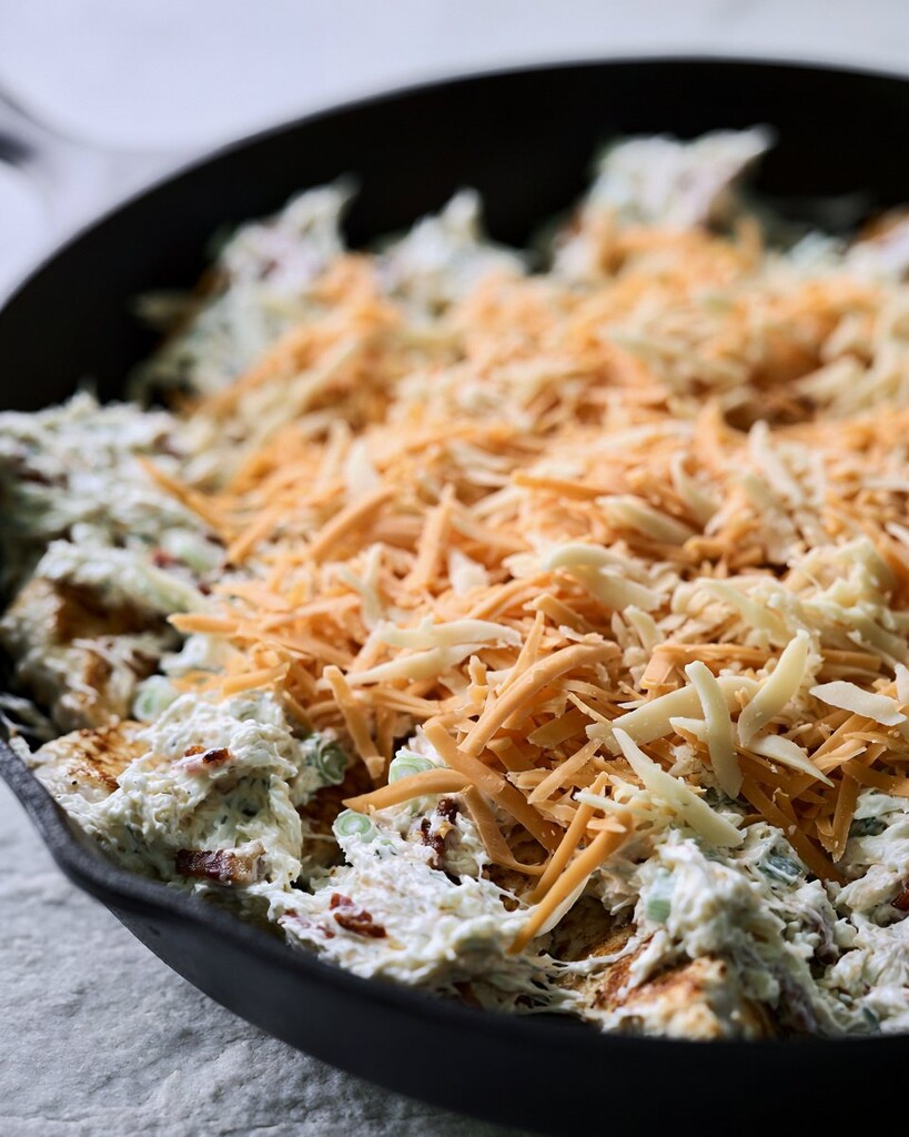 Seared chicken tenders in a skillet topped with cream cheese mixture and a thick layer of grated cheese