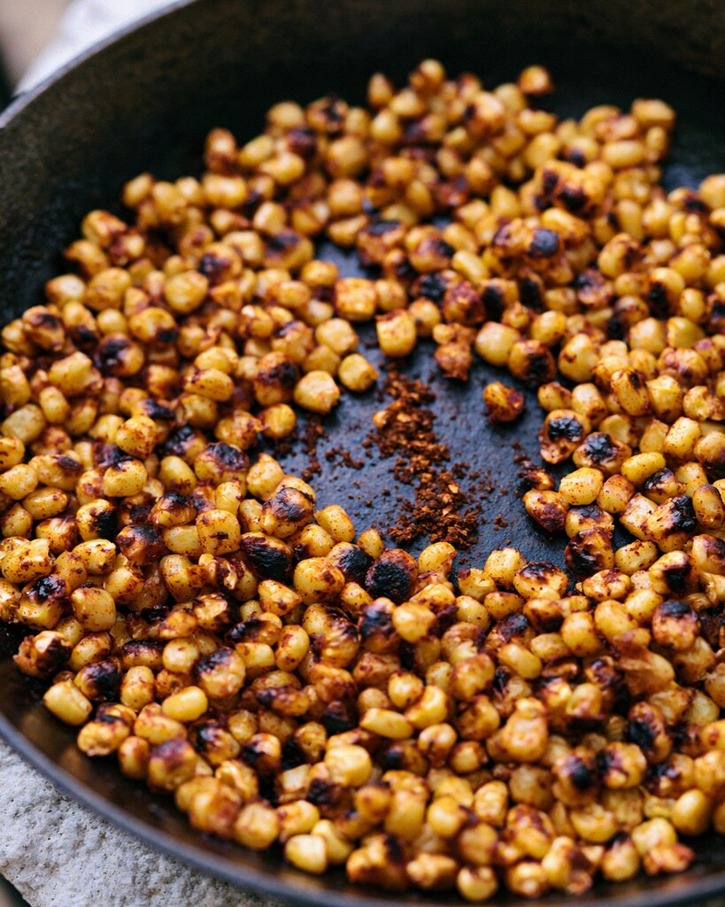 Sweet corn kernels browning and charring in a dark skillet with leftover spices