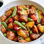 Pineapple teriyaki chicken with snap peas and edamame served in a white bowl topped with sesame seeds