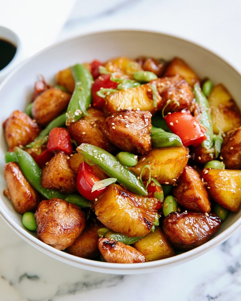 Pineapple teriyaki chicken with snap peas and edamame served in a white bowl topped with sesame seeds