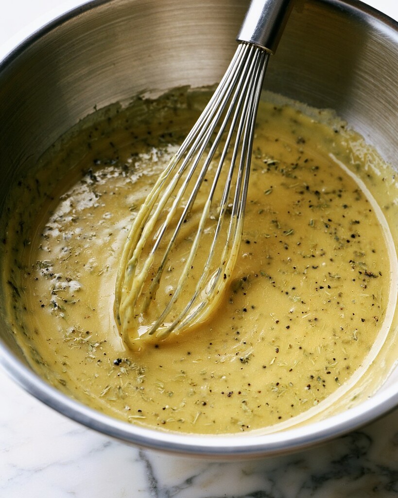 A creamy pepperoncini vinaigrette being whisked together with herbs and spices in a metal mixing bowl