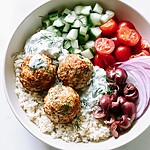 Baked Greek turkey meatballs served over white quinoa with fresh tomatoes, cucumbers, Kalamata olives, and a dollop of tzatziki
