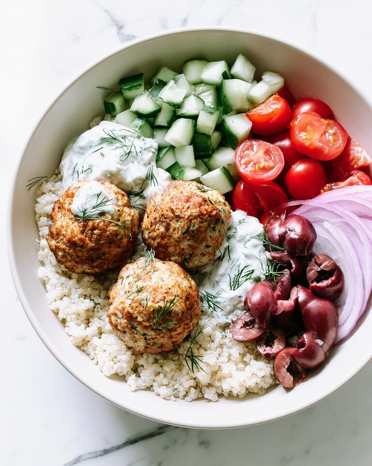 Baked Greek turkey meatballs served over white quinoa with fresh tomatoes, cucumbers, Kalamata olives, and a dollop of tzatziki