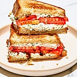 Heirloom tomato sandwich with whipped cottage cheese cut in half on a board