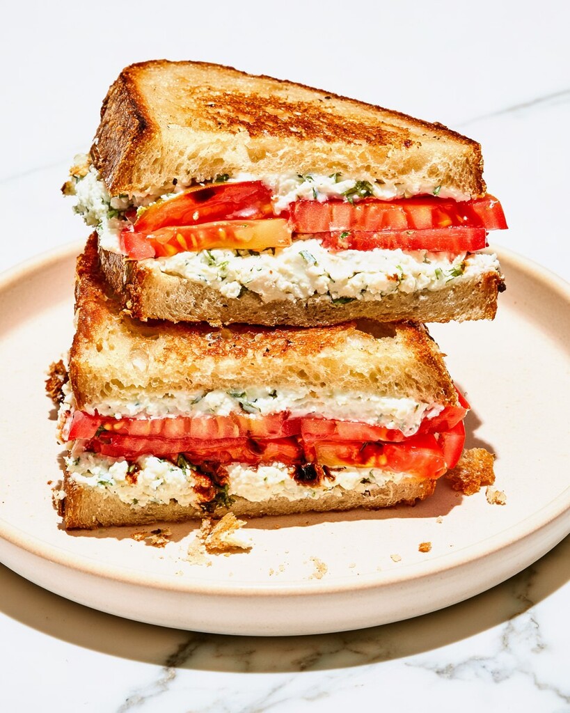 Heirloom tomato sandwich with whipped cottage cheese cut in half on a board