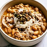 White chicken chili in a ceramic bowl topped with shredded cheese, sour cream, and toasted pumpkin seeds